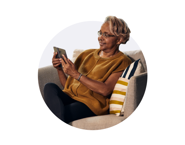 A senior woman sitting on a couch smiling at her device