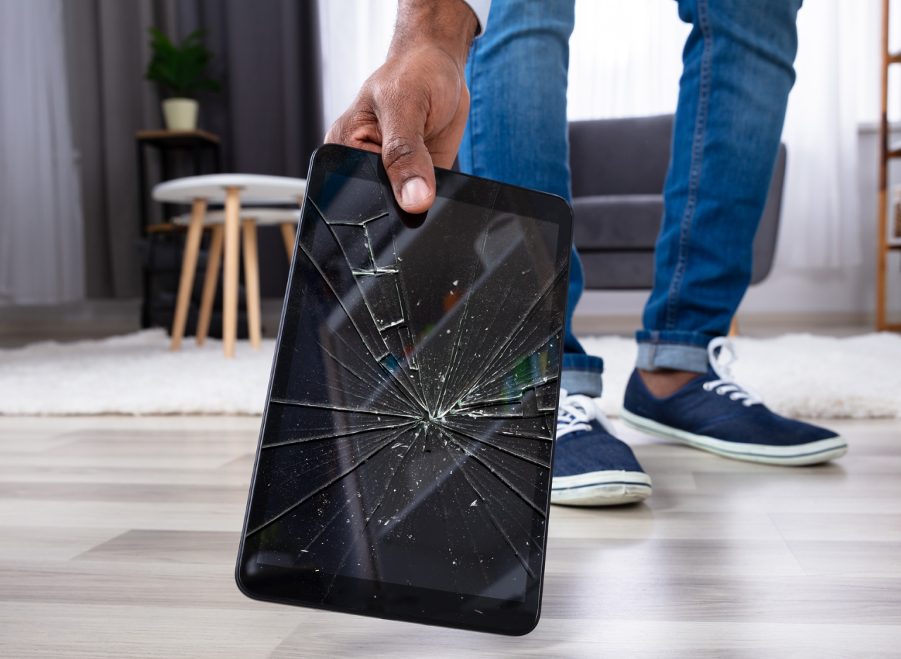 A person picking up a dropped tablet with a cracked screen