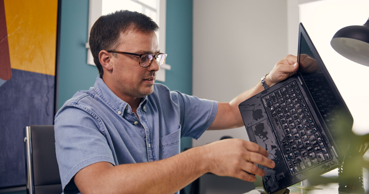 A man holding a laptop at an angle to remove spilled water