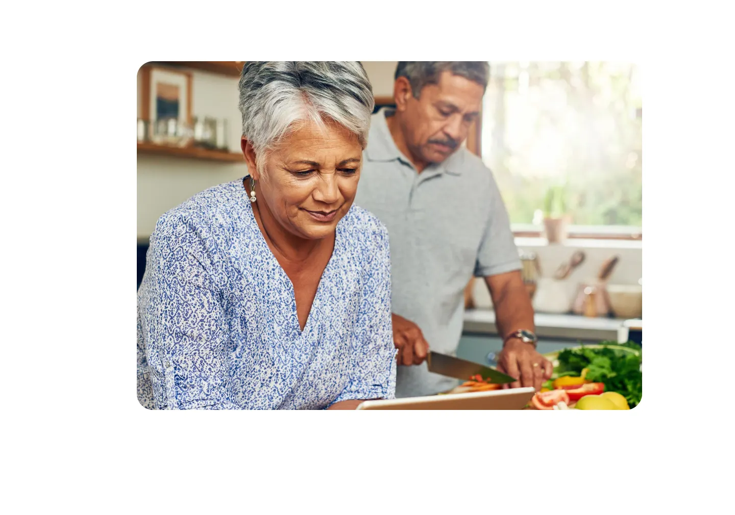woman holding tablet in kitchen man cutting vegetables