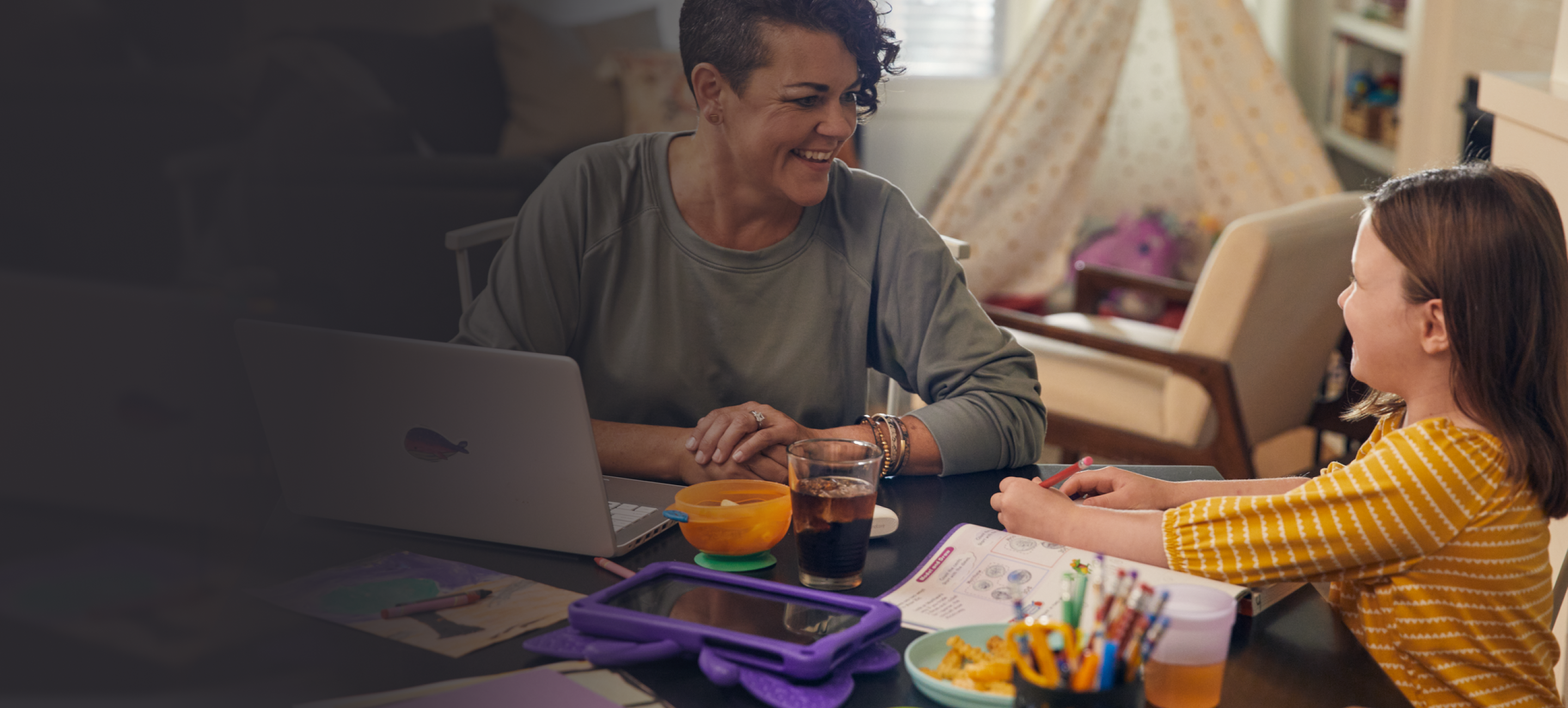 Mother working at laptop talking with daughter using tablet