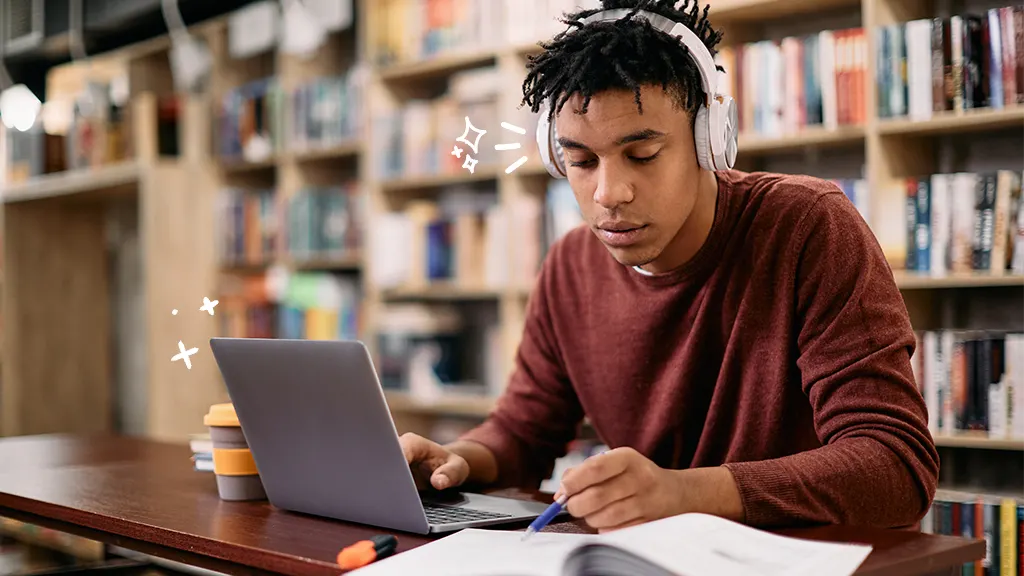 Student studies in library while listening to music on headphones and using a laptop. 