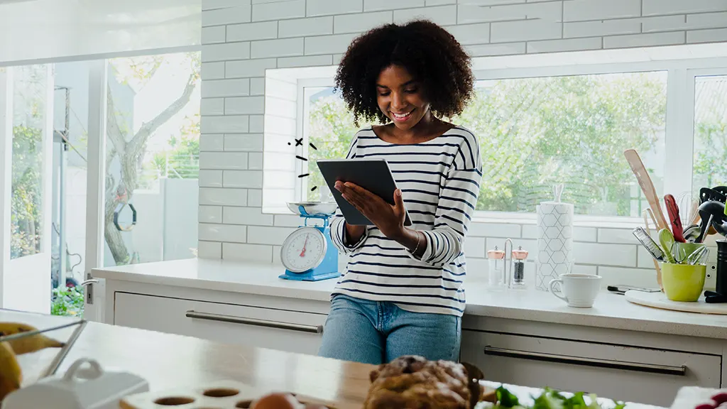 young woman in the kitchen looking at her old Android tablet 