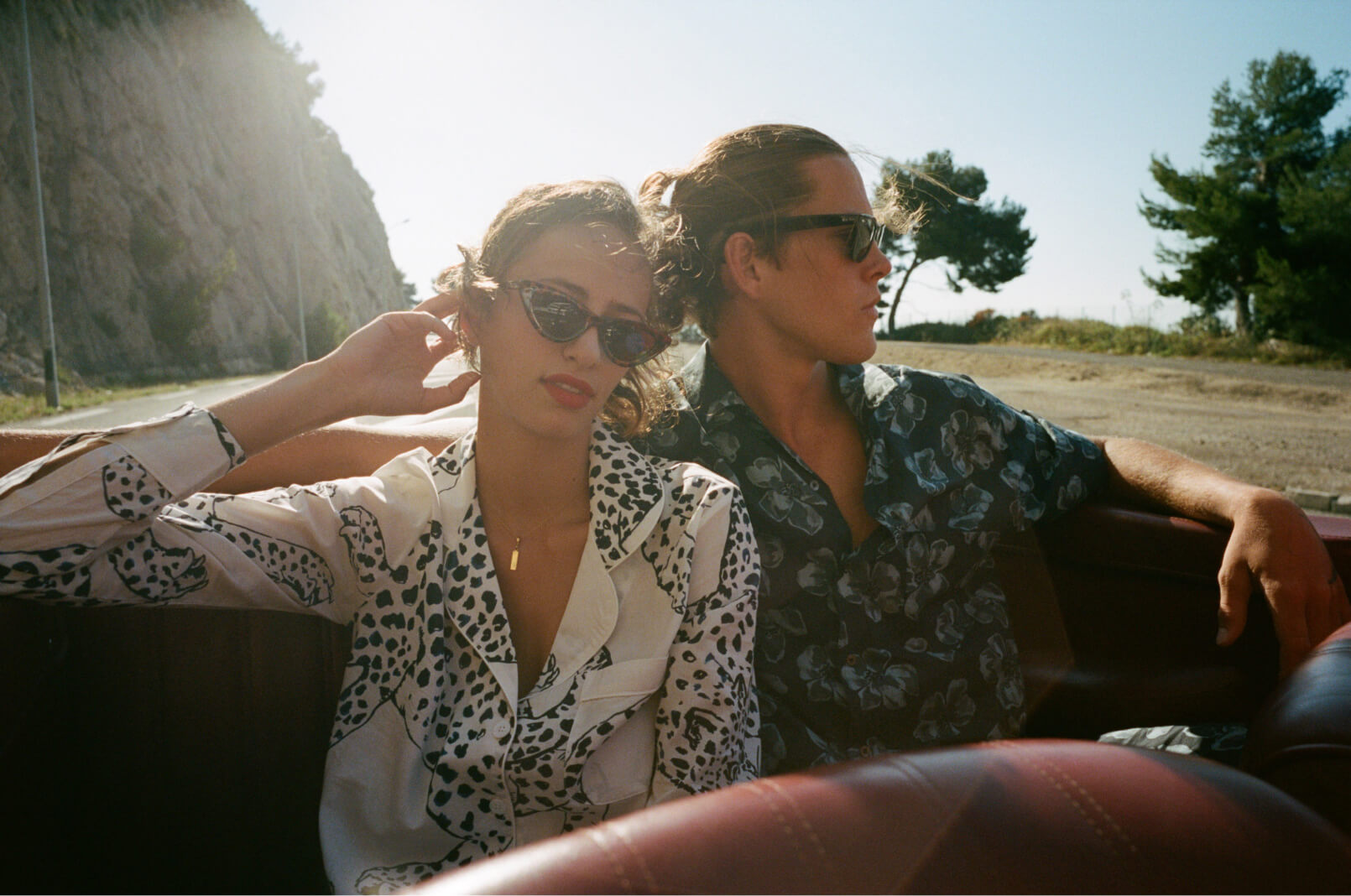 A woman and a man sitting outside in a convertible on a sunny day wearing Desmond & Dempsey tops with abstract prints.