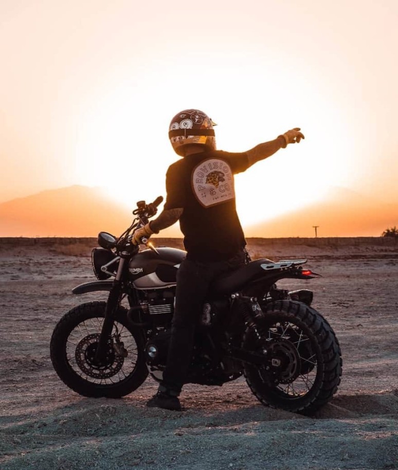 A motorcycle rider points off into the setting sun