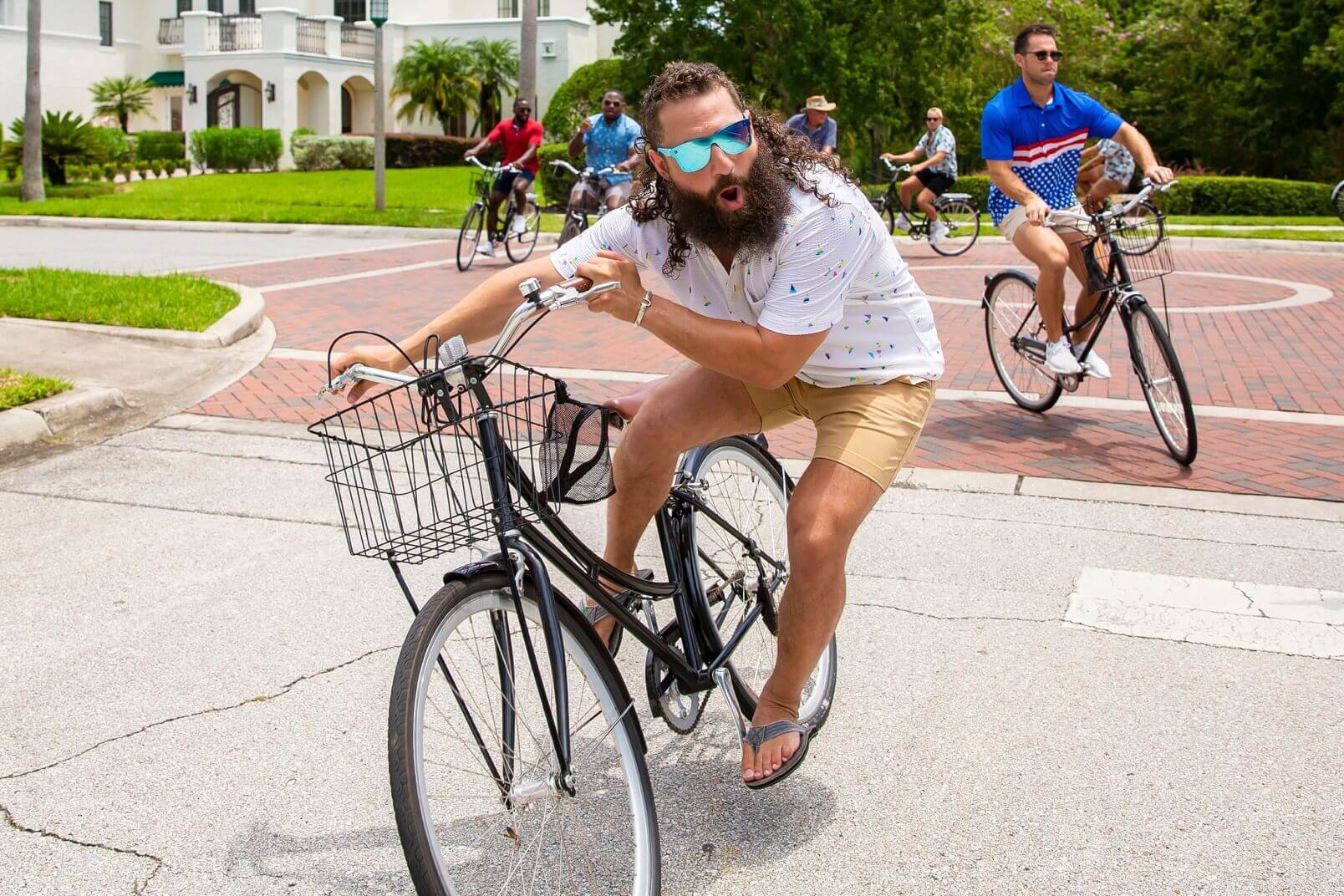 A man in flip-flops, khaki shorts, and a white shirt aggressively rides a bike, showing you can be very active while wearing Chubbies.