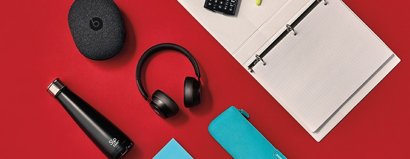Headphones, a water bottle, and a binder from Staples are laid neatly on a flat surface.