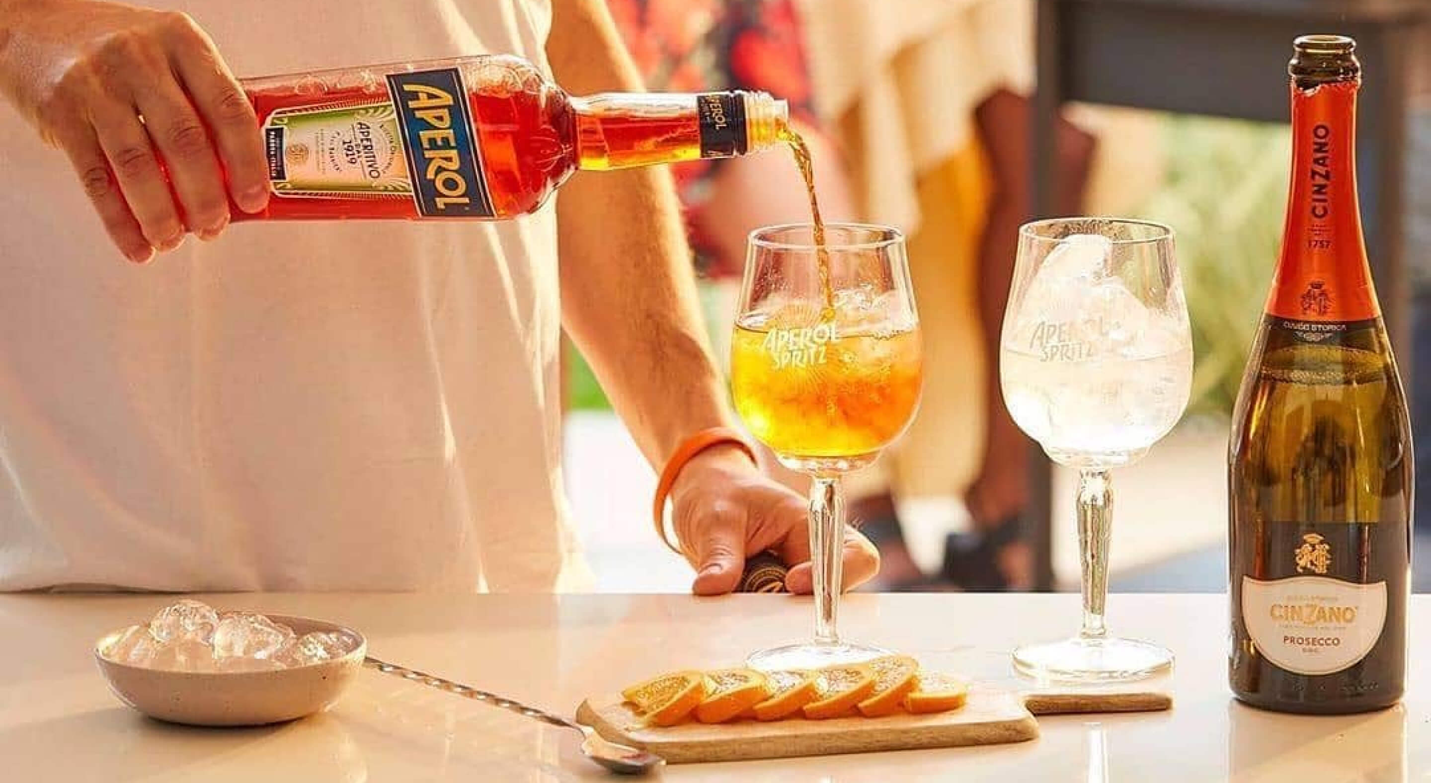 A bottle of Aperol being poured into a tall, stemmed glass filled with ice