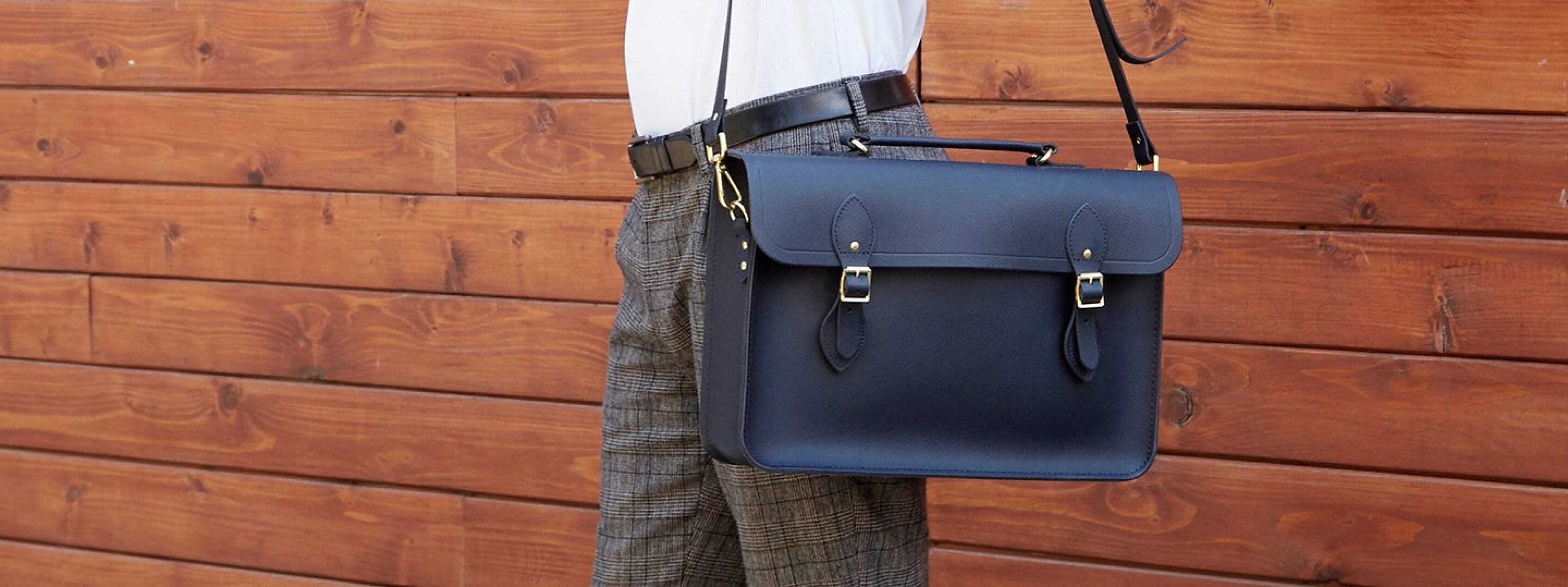 A black satchel with gold colored buckels hangs over a person’s shoulder.