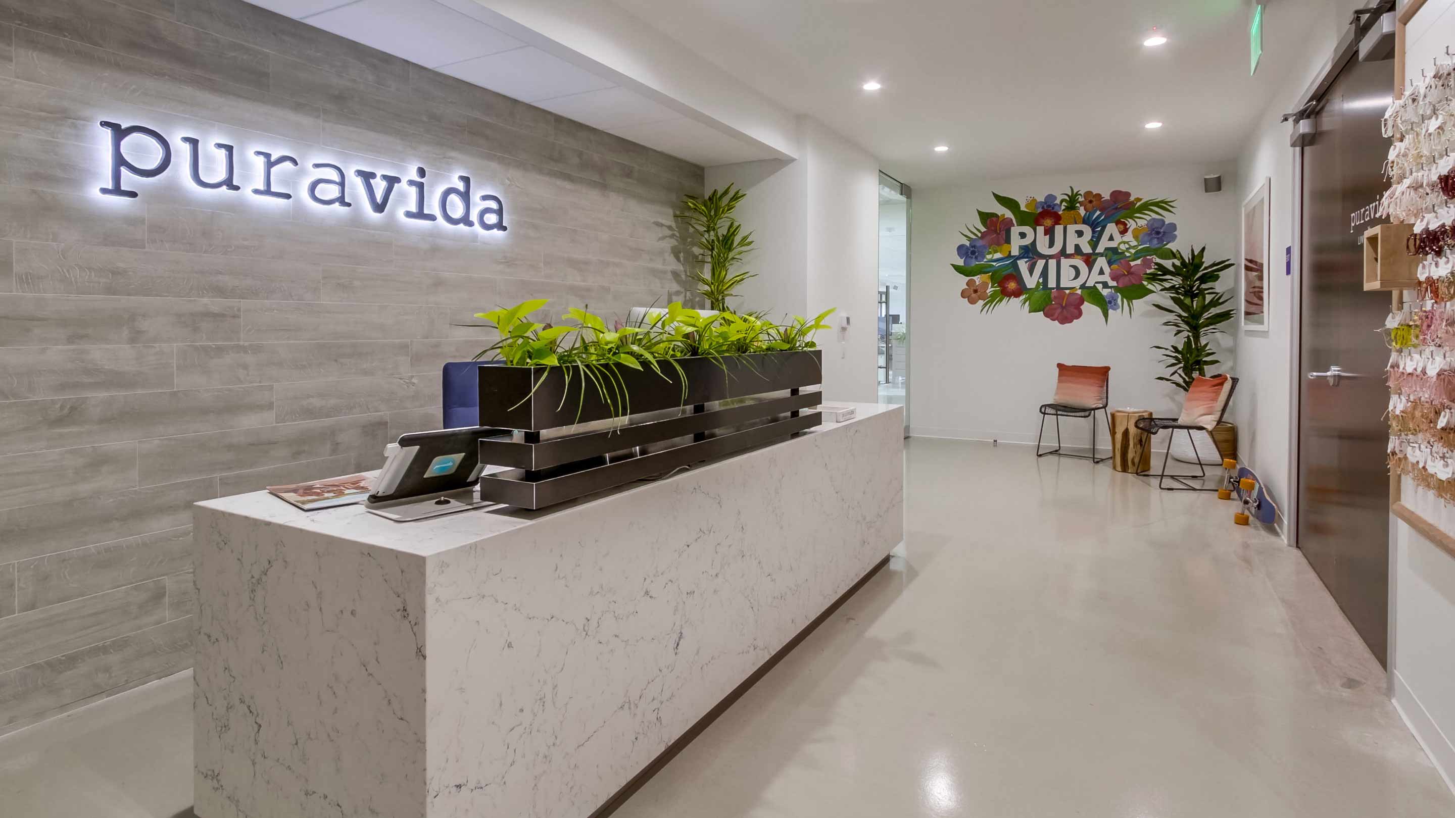 The reception area of Pura Vida’s office decorated with plants, a marble reception desk and a large floral mural.