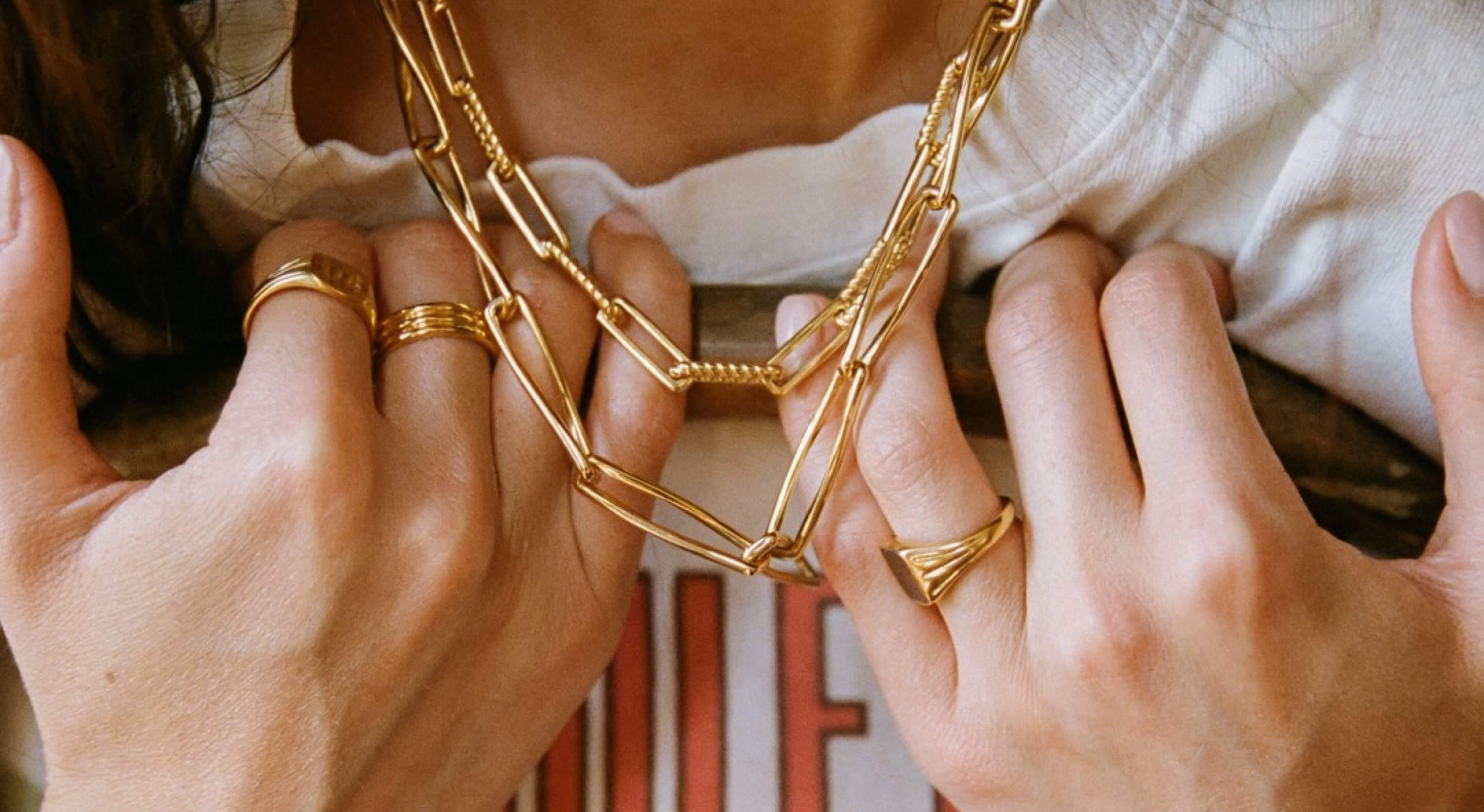 Woman wearing two golden link Missoma chains around her neck with three matching golden rings.