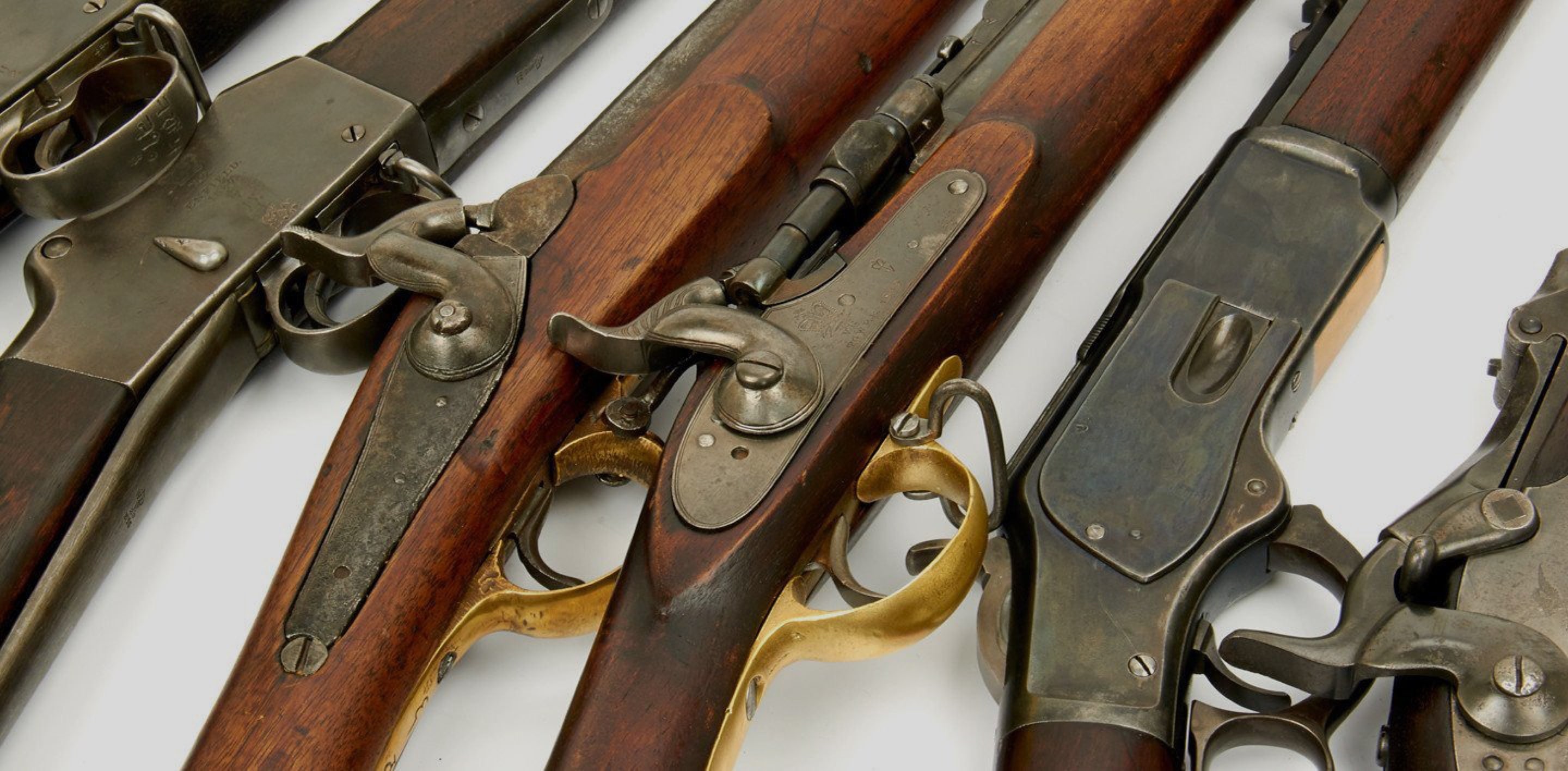 Antique military rifles are displayed in horizontal, laid across a white surface.