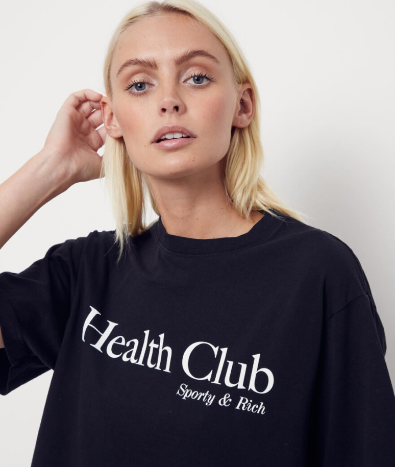 A girl with straight blond hair wearing a black shirt that says "Health Club".