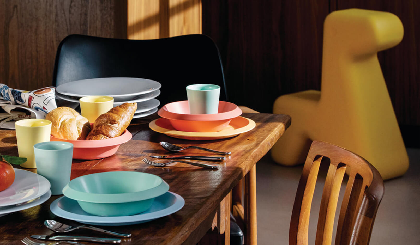 A wooden table set with pastel coloured plates, cups, and bowls.