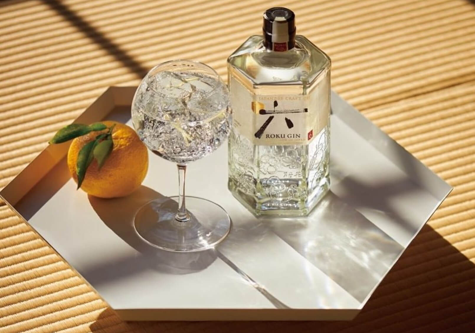 A bottle of Roku gin on a hexagonal tray with a stemmed glass and an orange