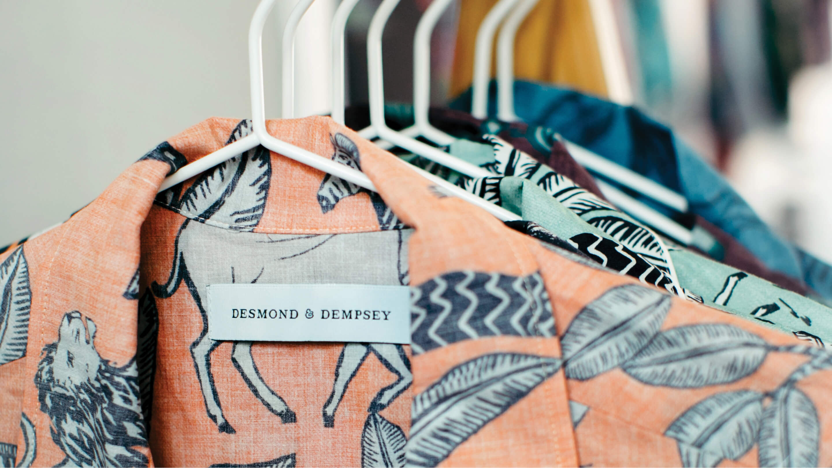 The collar of an orange shirt with black printed animals and plants and  Desmond & Dempsey printed on the label.