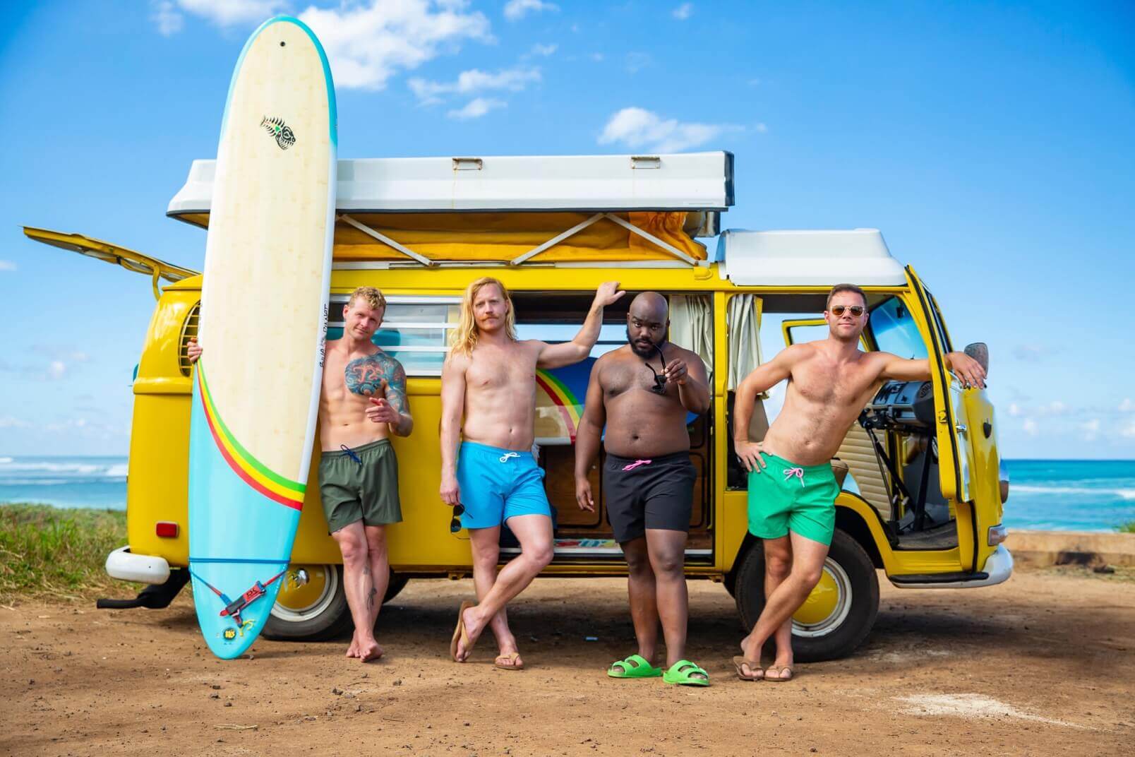 Four men pose with a surfboard in front of a van. They’re all wearing different coloured Chubbies.