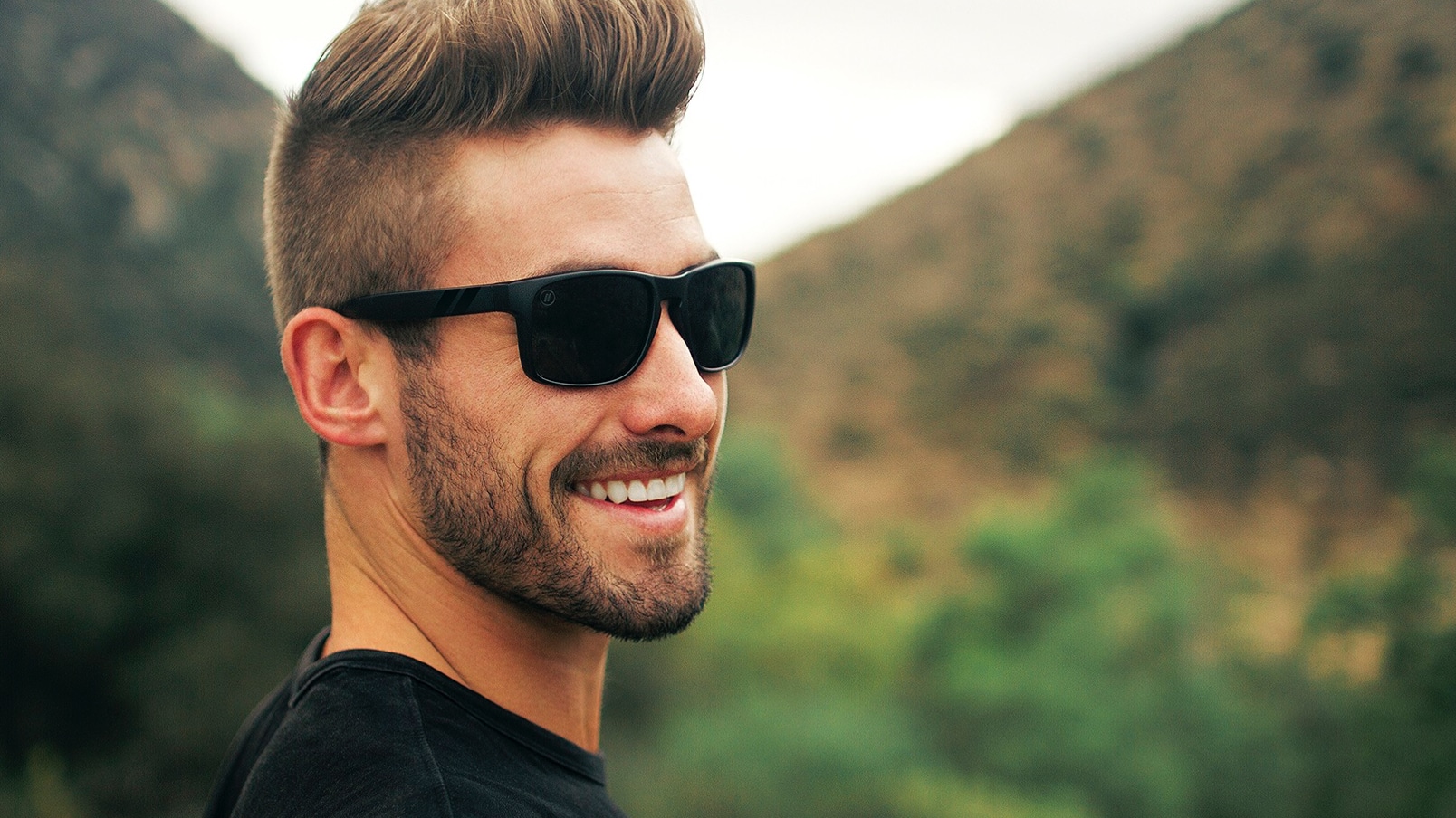 A man smiles while wearing a pair of black Blenders Eyewear sunglasses.