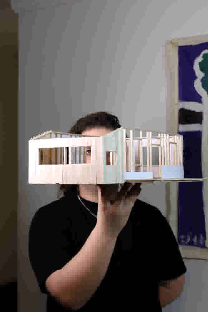 A miniature house is held up by the artist. 