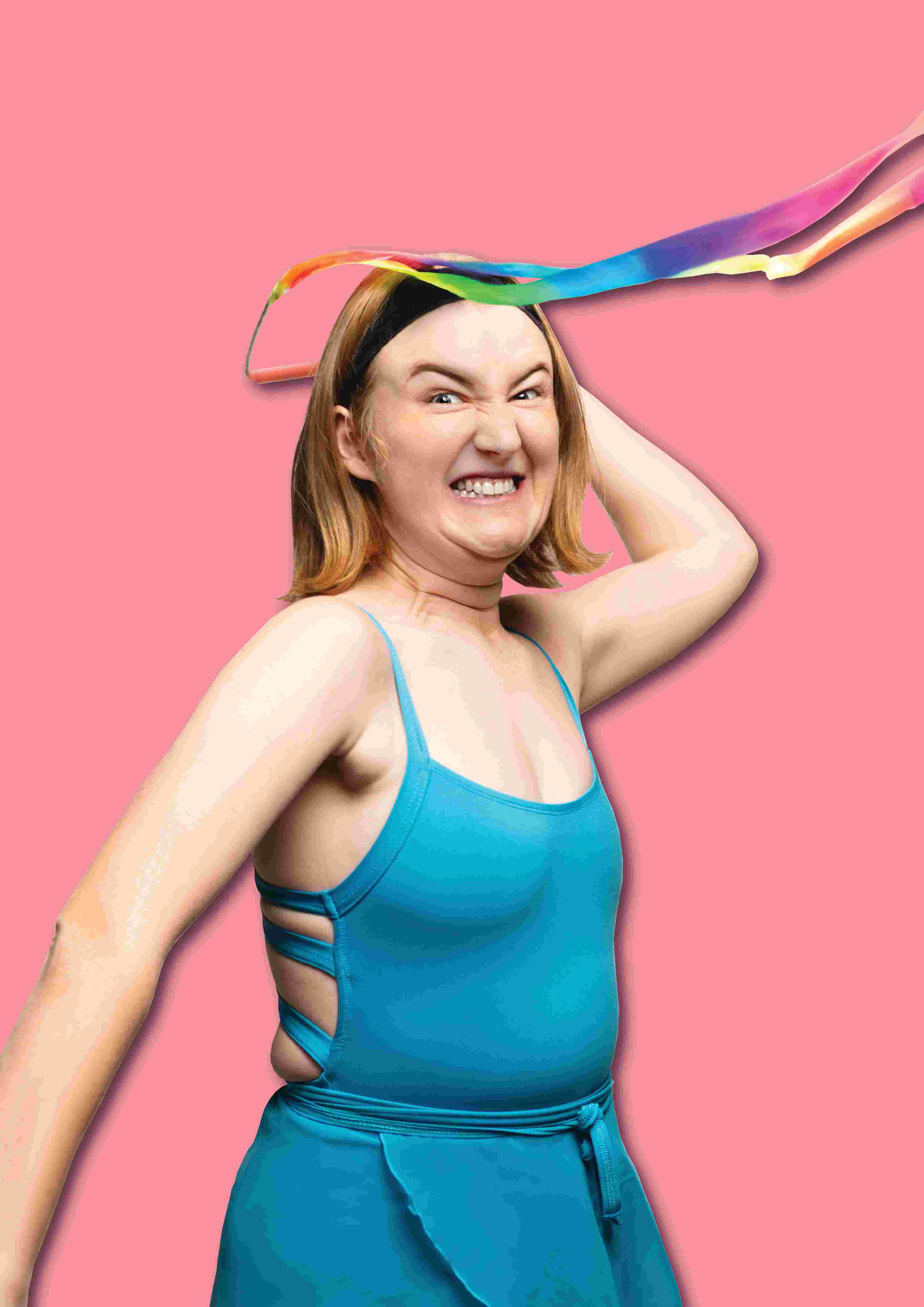 A woman wearing a bright blue leotard angrily throws a rainbow coloured ribbon towards the viewer.