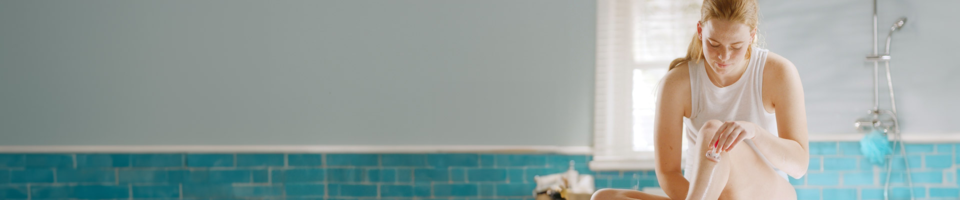 A woman shaving her leg with a Gillette Venus razor while sitting on a bathroom counter.