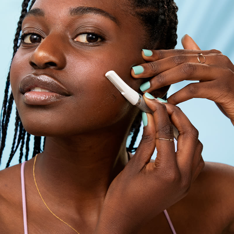 Young woman shaving her face with dermaplane razor