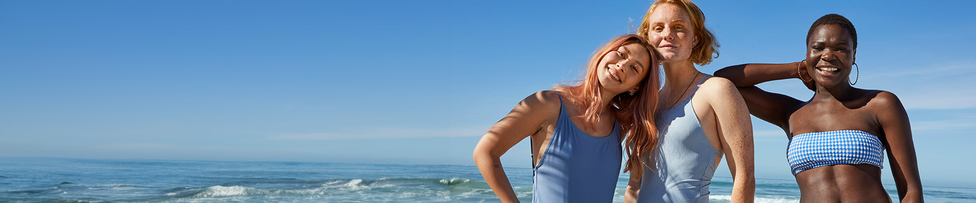 Three women in blue swimming suits on the beach posing and smiling.