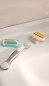 Silver refillable Gillette Venus razor with a detached yellow razor head and blue razor head next to it