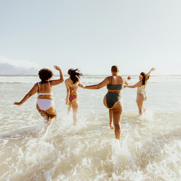 Four women joyfully run into the ocean waves on a sunny day, enjoying a fun day at the beach.