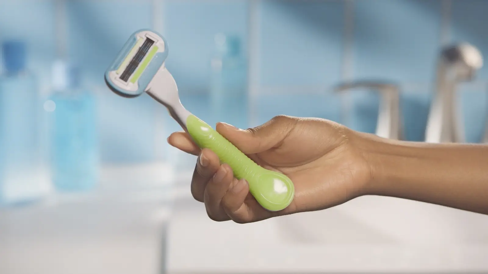 Women hand holding a green razor with an oval razor head