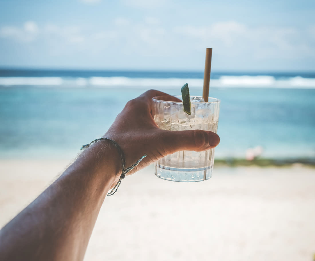 Picture of a hand holding a cocktail in front of a beach