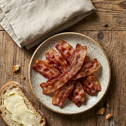 Crispy Bacon on a plate next to buttered slice of bread