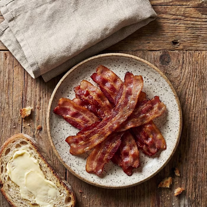 Crispy Bacon on a plate next to buttered slice of bread
