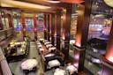 A spacious, upscale restaurant with high wooden columns, elegant lighting, white tablecloths, and large windows overlooking a brightly lit city street at night. Tables and booths are neatly arranged on two levels.