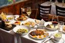 A table set for two with plates of French cuisine, including roast chicken, burgers, fries, vegetables, bread, wine glasses with red and white wine, and side dishes in a cozy restaurant setting.