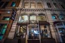 Nighttime street view of the entrance to Tarallucci e Vino, an Italian restaurant with large arched windows, glass doors, and a brown awning, set in a historic building with ornate architectural details.