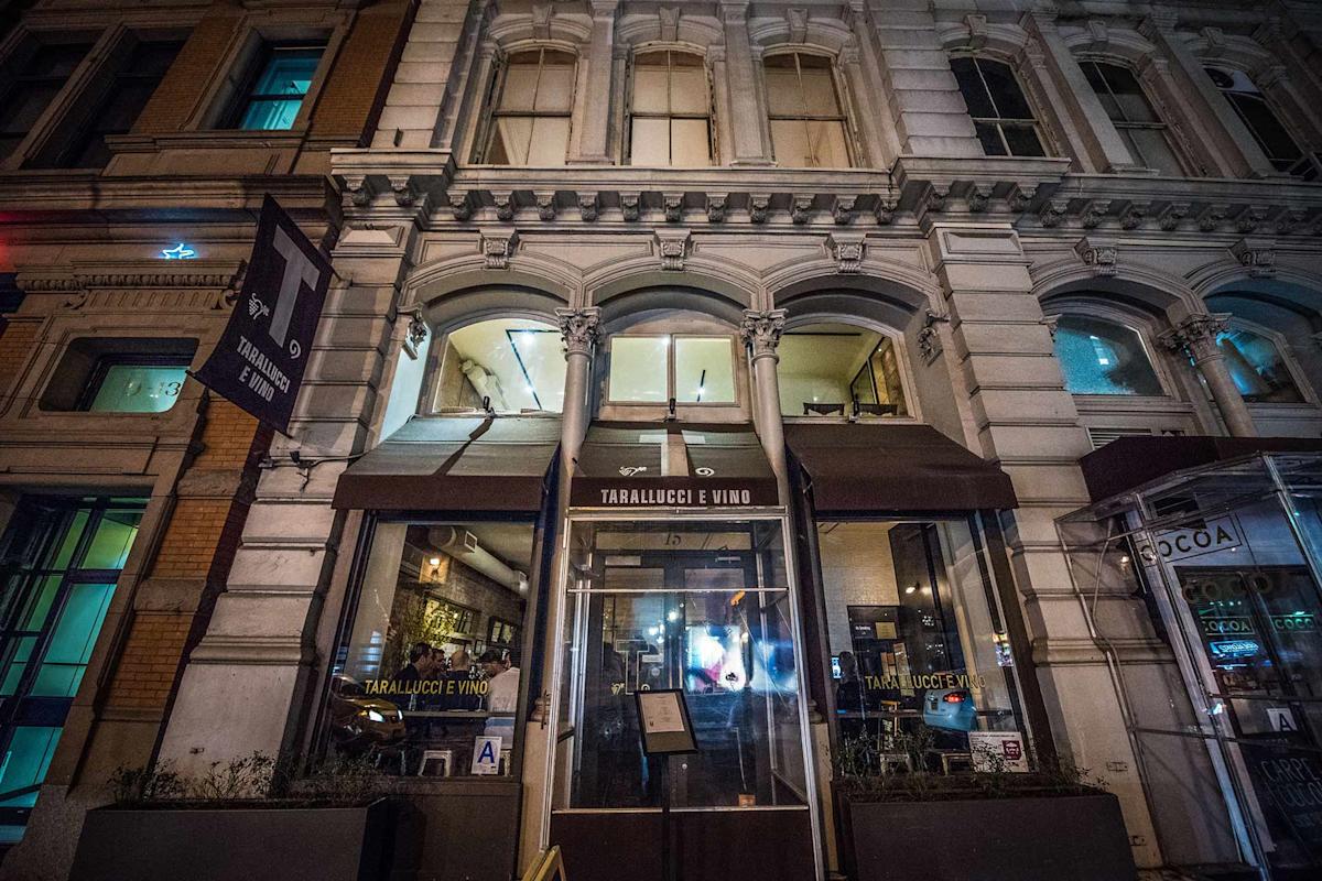 Nighttime street view of the entrance to Tarallucci e Vino, an Italian restaurant with large arched windows, glass doors, and a brown awning, set in a historic building with ornate architectural details.