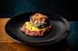 A gourmet dish featuring a stuffed roasted poblano pepper topped with shredded cheese, served on a bed of green sauce and red tomato sauce, presented on a black plate against a dark background.