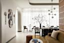 A modern living and dining area with neutral tones, abstract wall art, a long dining table with black chairs, a decorative indoor tree, and large windows with sheer white curtains allowing natural light in.