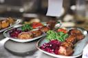 Two plates of grilled meat skewers served with fresh parsley, sliced tomato, and a side of red cabbage salad on a metal counter in a restaurant kitchen.