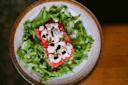 A salad with a slice of watermelon topped with crumbled goat cheese and drizzled with balsamic glaze, surrounded by fresh arugula on a white ceramic plate.