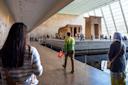 Several people walk and observe the ancient Egyptian Temple of Dendur housed in a bright, spacious gallery with large windows at the Metropolitan Museum of Art in New York City.