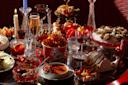 A lavish table setting with various dishes, including ramen, oysters on ice, cheese, olives, nuts, and fruits. Glasses of champagne and red wine are surrounded by lit candles, creating an elegant dining atmosphere.