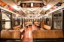 Vintage subway car interior with wooden benches, metal poles, and advertisements from the mid-20th century on walls and ceiling. The car has a nostalgic and historical ambiance, reflecting classic transit design.