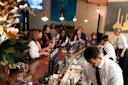 A group of people socialize and enjoy drinks around a busy bar, while bartenders prepare cocktails and serve customers in a lively, modern setting.