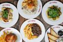 Six plates of food from Café D’Anvers on a wooden table, featuring fries, hamburgers, toast, beef stew, puff pastry, roasted potatoes, and salad, each attractively arranged on white plates.