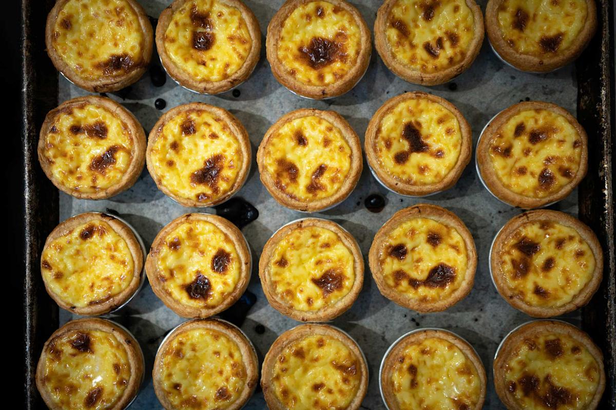Rows of golden-brown egg tarts neatly arranged on a baking tray, each with a slightly browned top and flaky pastry crust, creating a visually appealing pattern.