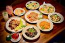 A wooden table filled with various Asian dishes, including shrimp, pork, vegetables, tofu, tea, and colorful drinks, all neatly arranged and garnished with herbs.