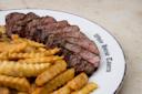 A plate from "White House Tavern" with slices of medium-rare steak and crinkle-cut fries. The steak is juicy and slightly charred, while the fries are golden and crispy.