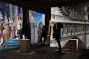 People view photographs and projections of historical architecture and paintings in a dimly lit exhibit. The images include ornate cathedral details and a scene of regal figures, enhancing the immersive cultural experience.